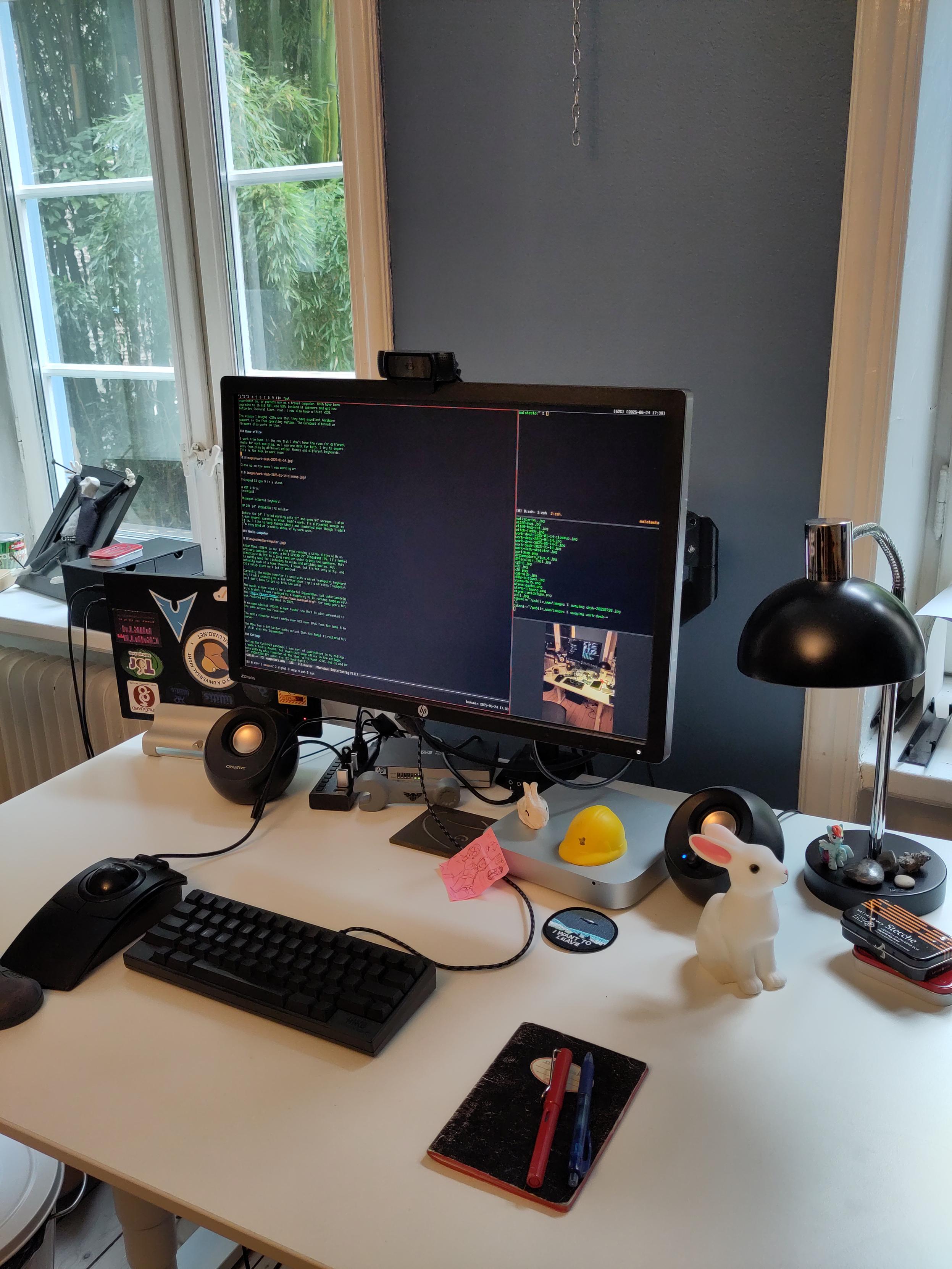 White desk with a large monitor, keyboard, trackpad and computers in
front of a blue wall and old-style windows.
